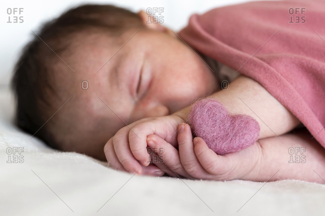Close-up of newborn baby girl with heart shape sleeping on bed in hospital