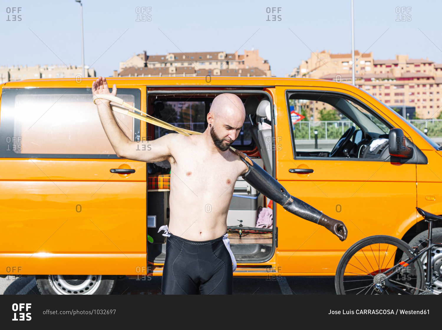 Bald adaptive athlete wearing artificial hand while standing against van