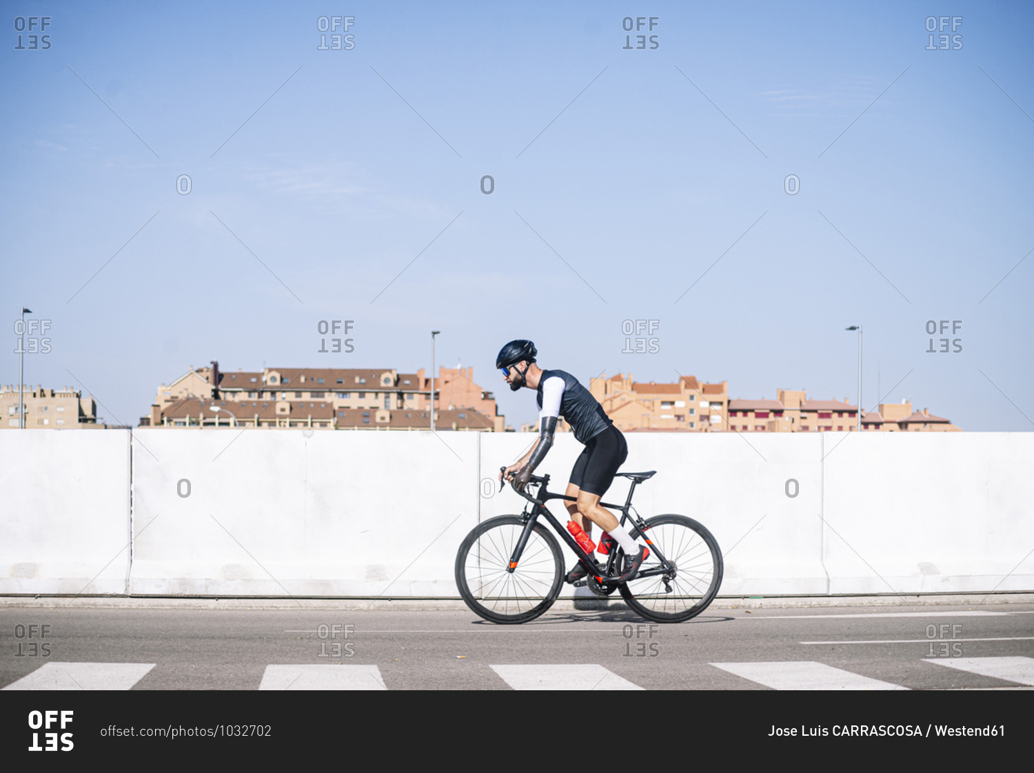 Male amputee cyclist riding bicycle on road against clear blue sky during sunny day