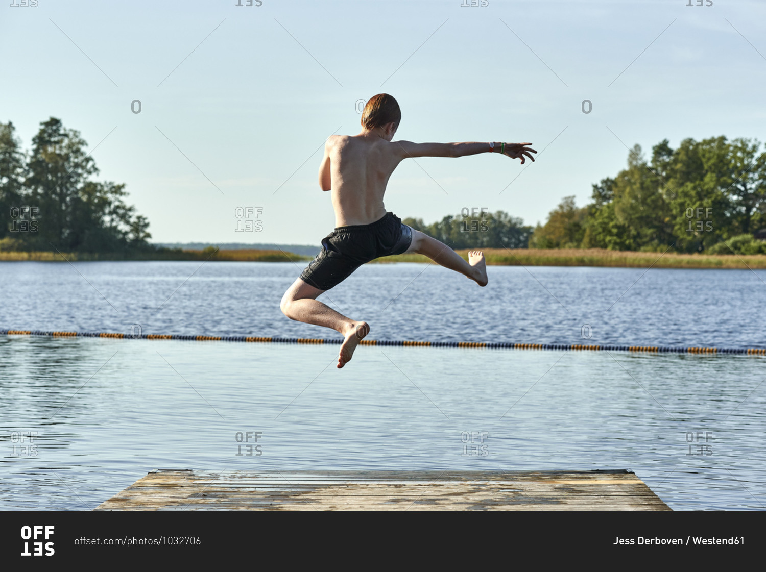 Redhead boy jumping into lake against clear sky