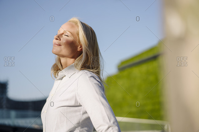 Contented beautiful blond businesswoman soaking sunlight in city