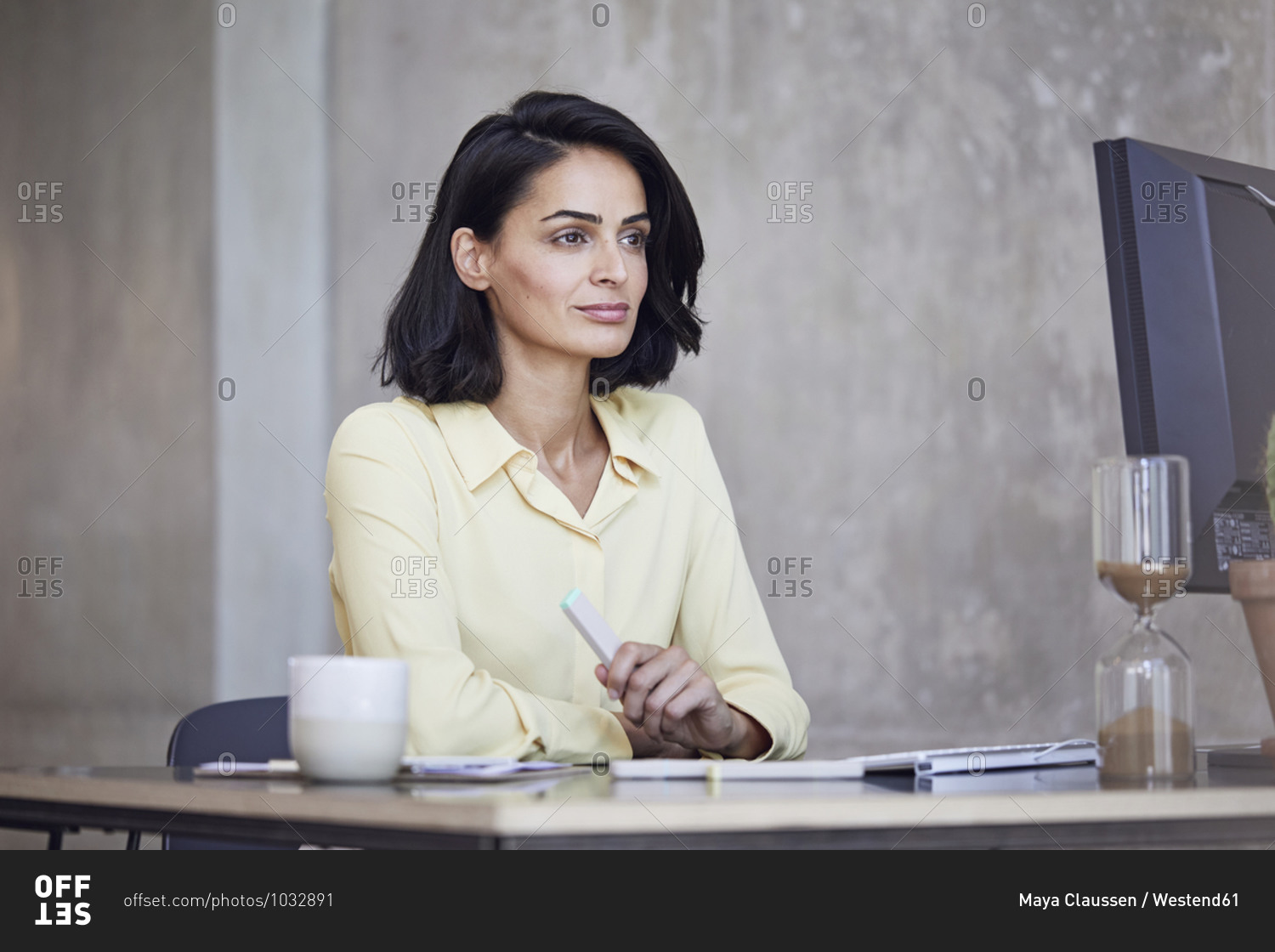 Thoughtful female entrepreneur looking away while sitting at desk against wall in office