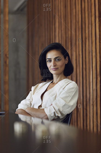 Serious businesswoman with short hair sitting at desk against wooden wall in office