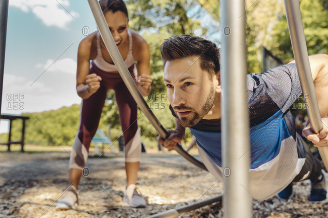Woman supporting man doing press-ups on a fitness trail