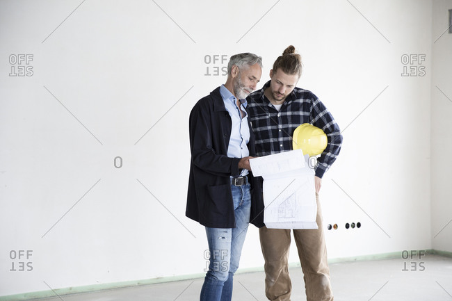 Architect and construction worker discussing blueprint while standing in empty house
