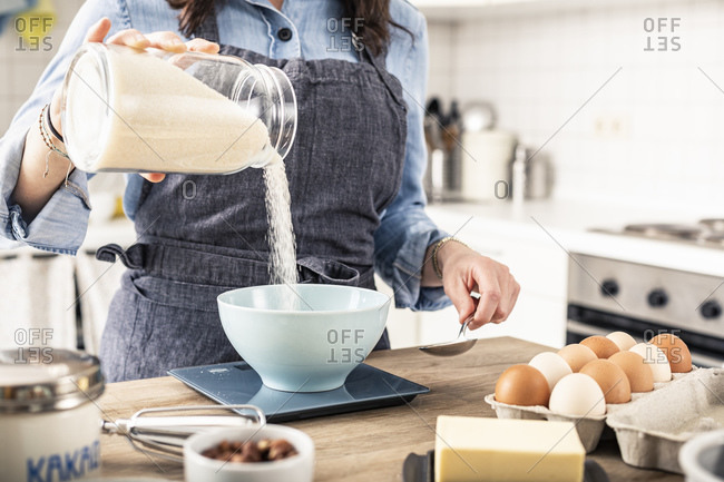 Woman weighing flour on kitchen scale for making cake at home