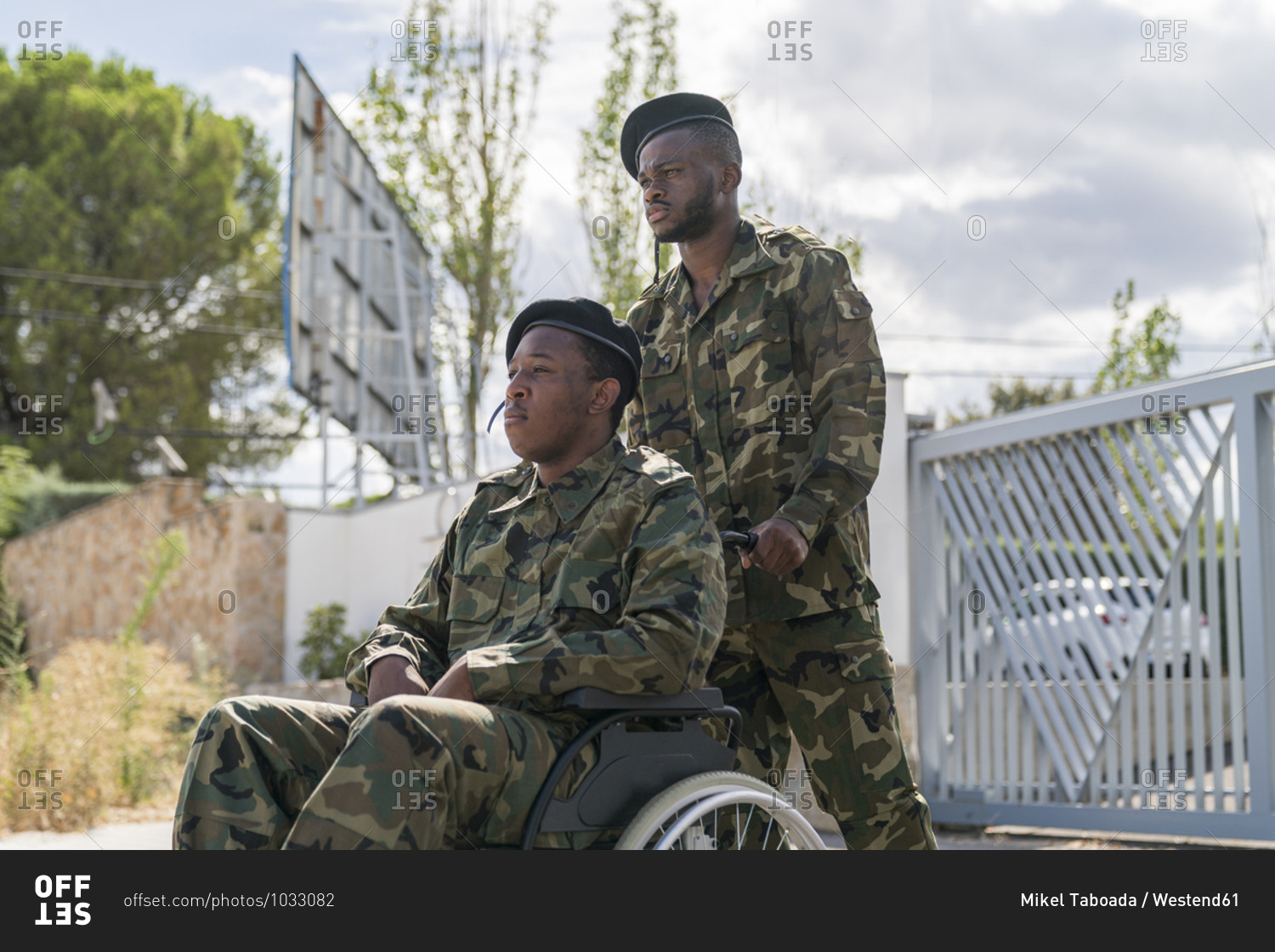 Serious army soldier helping another military officer sitting on wheelchair