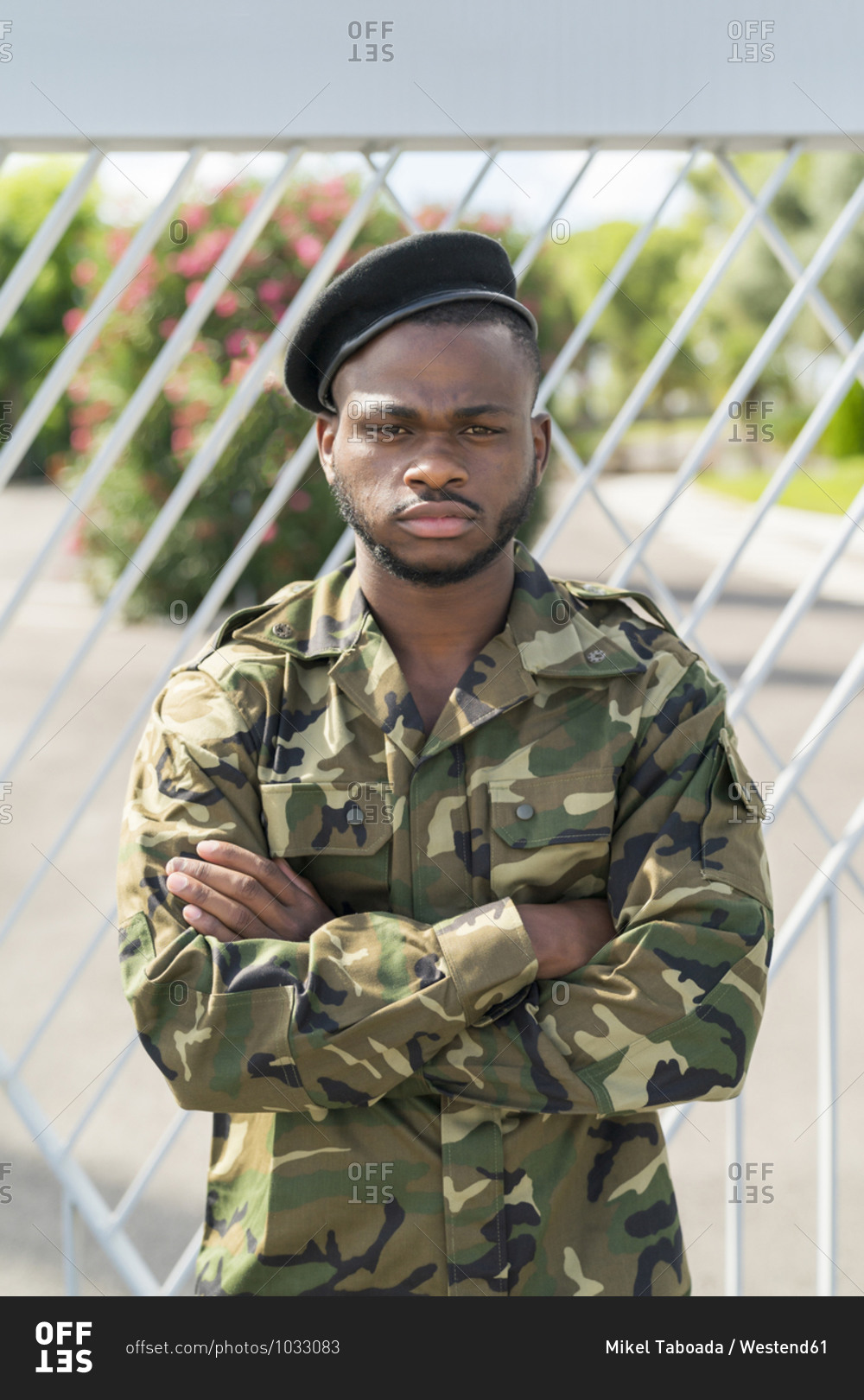 Army soldier standing with arms crossed against gate