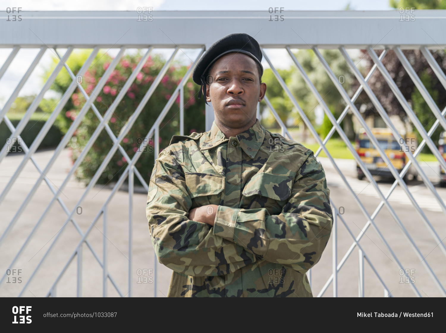 Confident army soldier standing with arms crossed against gate