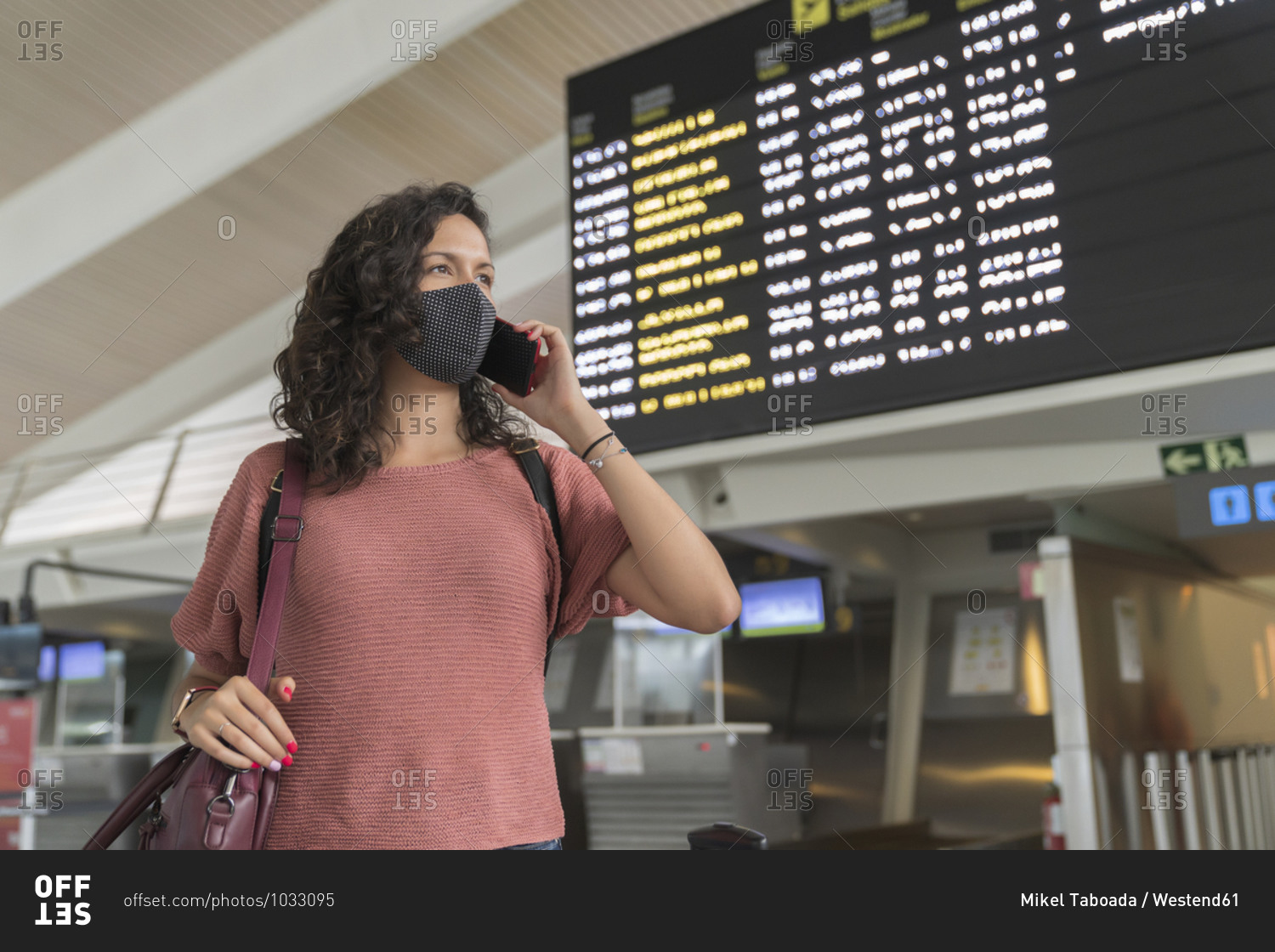 Young woman with protective face mask talking on smart phone while standing at airport