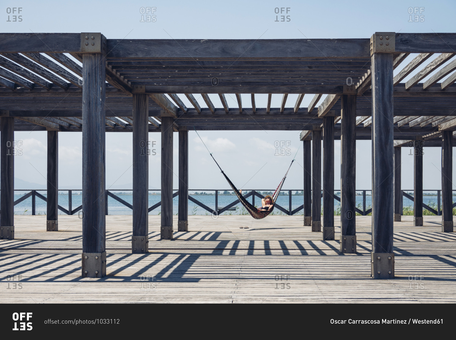 Woman lying in hammock hanging from metallic structure on boardwalk during sunny day