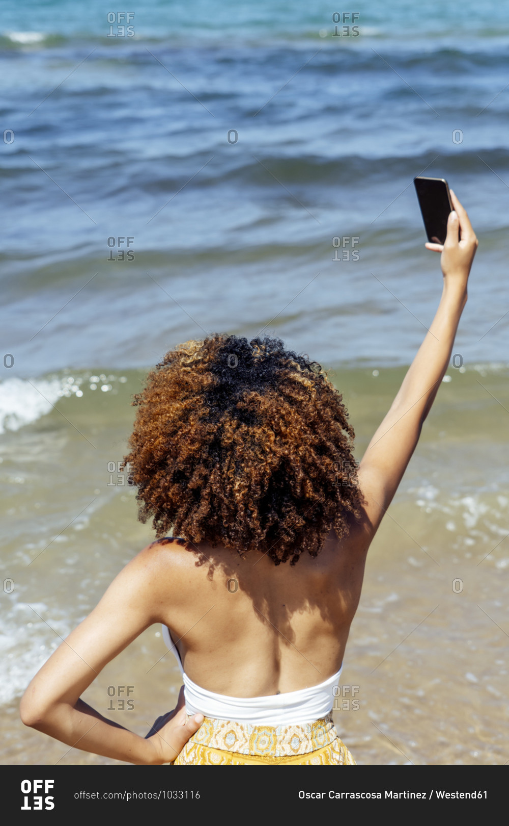 Young woman with curly hair taking selfie while standing in sea during summer