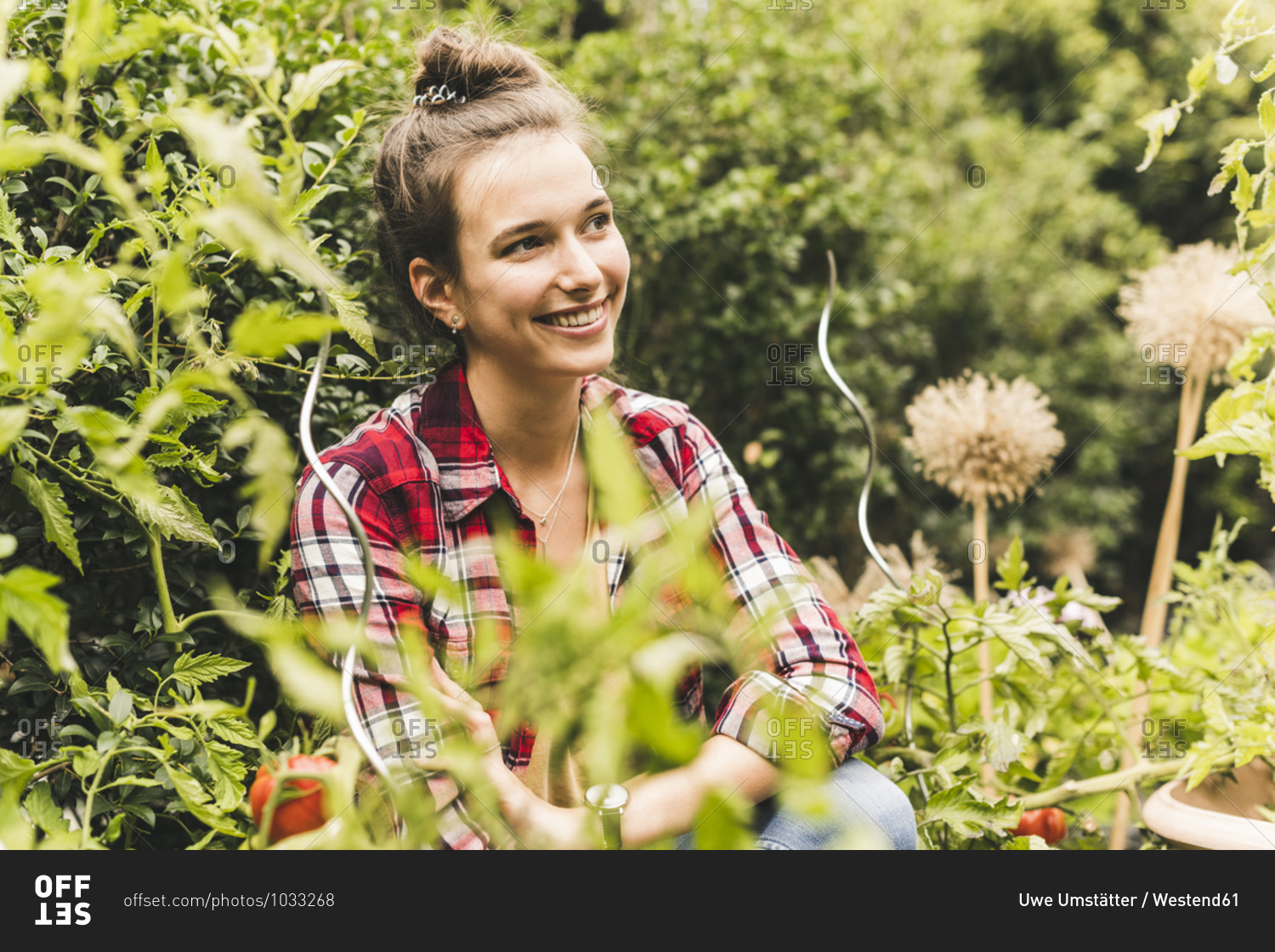 Smiling young woman looking away while sitting amidst plants in vegetable garden