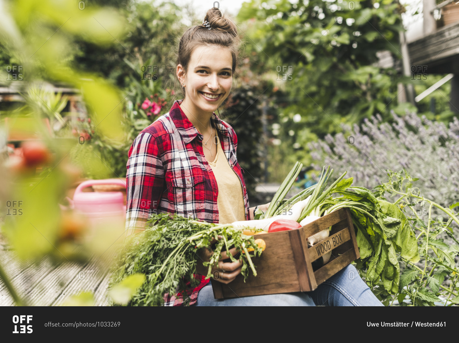 Smiling beautiful woman with vegetable crate sitting in community garden