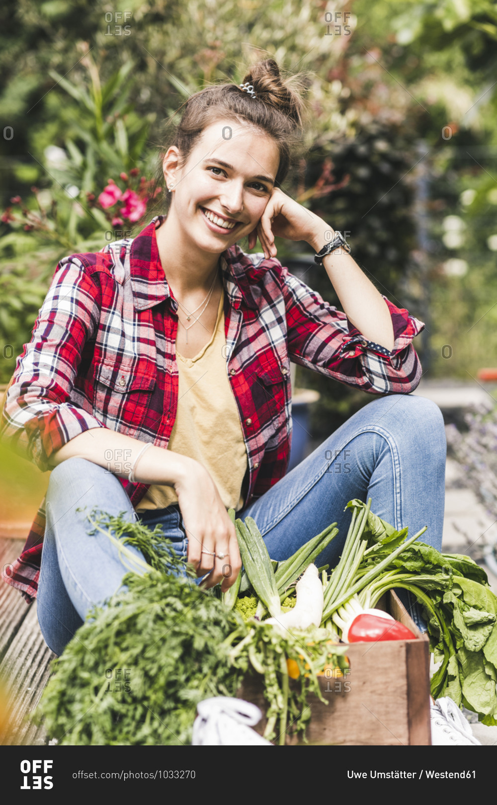 Smiling beautiful woman with vegetables sitting in community garden