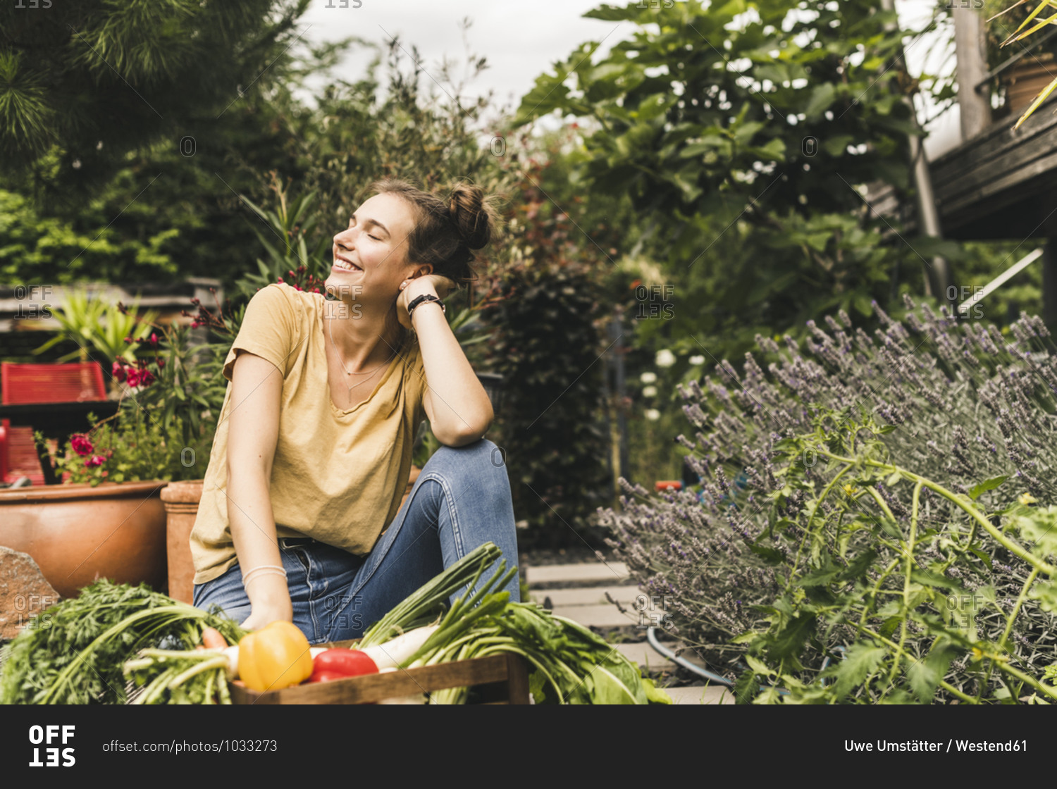 Young woman with eyes closed sitting by vegetables and plants in community garden