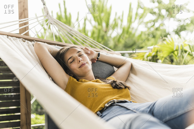 Beautiful woman with arms raised napping on hammock in yard