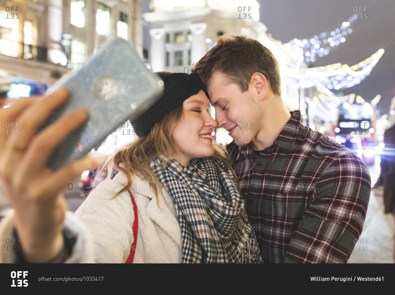 Close-up of romantic couple with face to face taking selfie in city at night