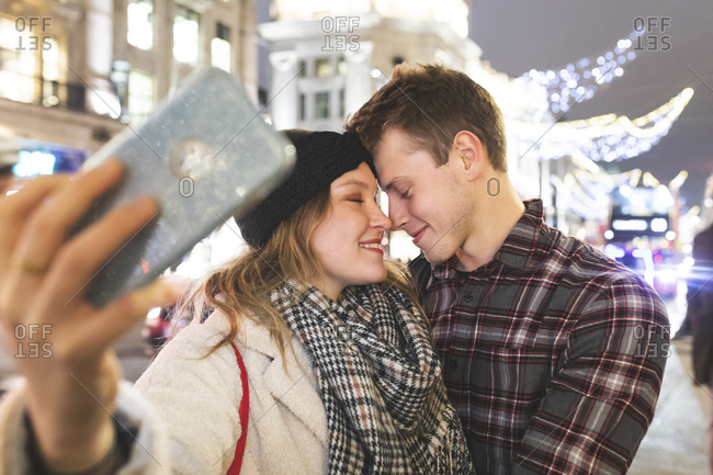 Close-up of romantic couple with face to face taking selfie in city at night