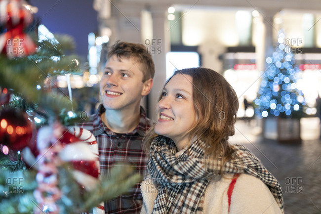 Happy young couple looking at Christmas tree and lights while standing in city