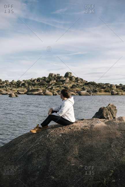 Young woman sitting on a rock in nature looking at a beautiful landscape