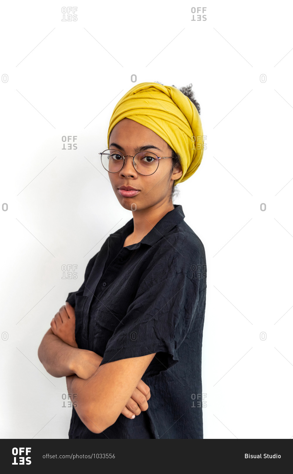 Close up of young mixed race woman with glasses and yellow scarf looking at camera while posing against white blank wall