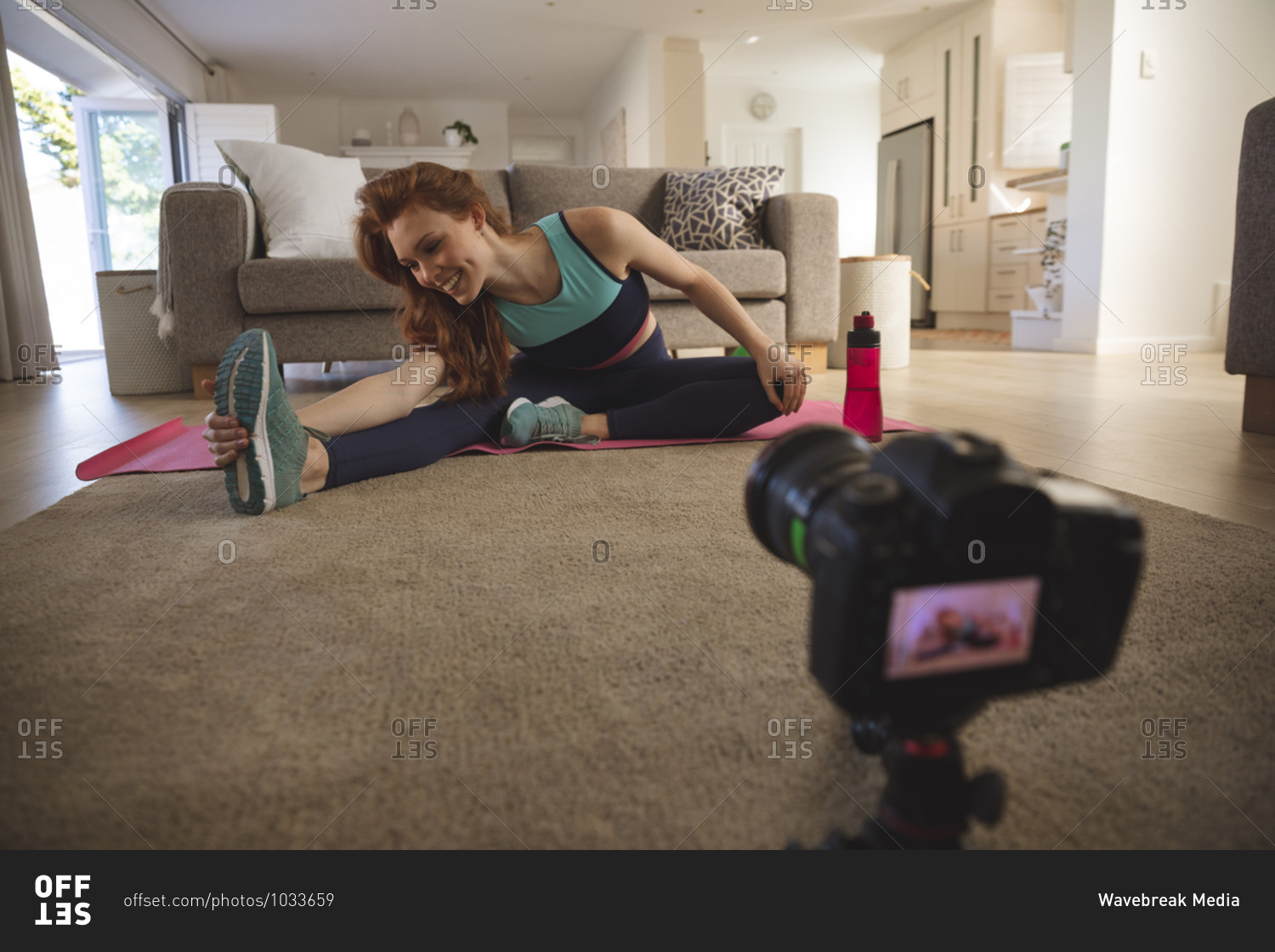 Caucasian woman spending time at home, in living room, exercising, stretching and recording it with a camera. Social distancing during Covid 19 Coronavirus quarantine lockdown.