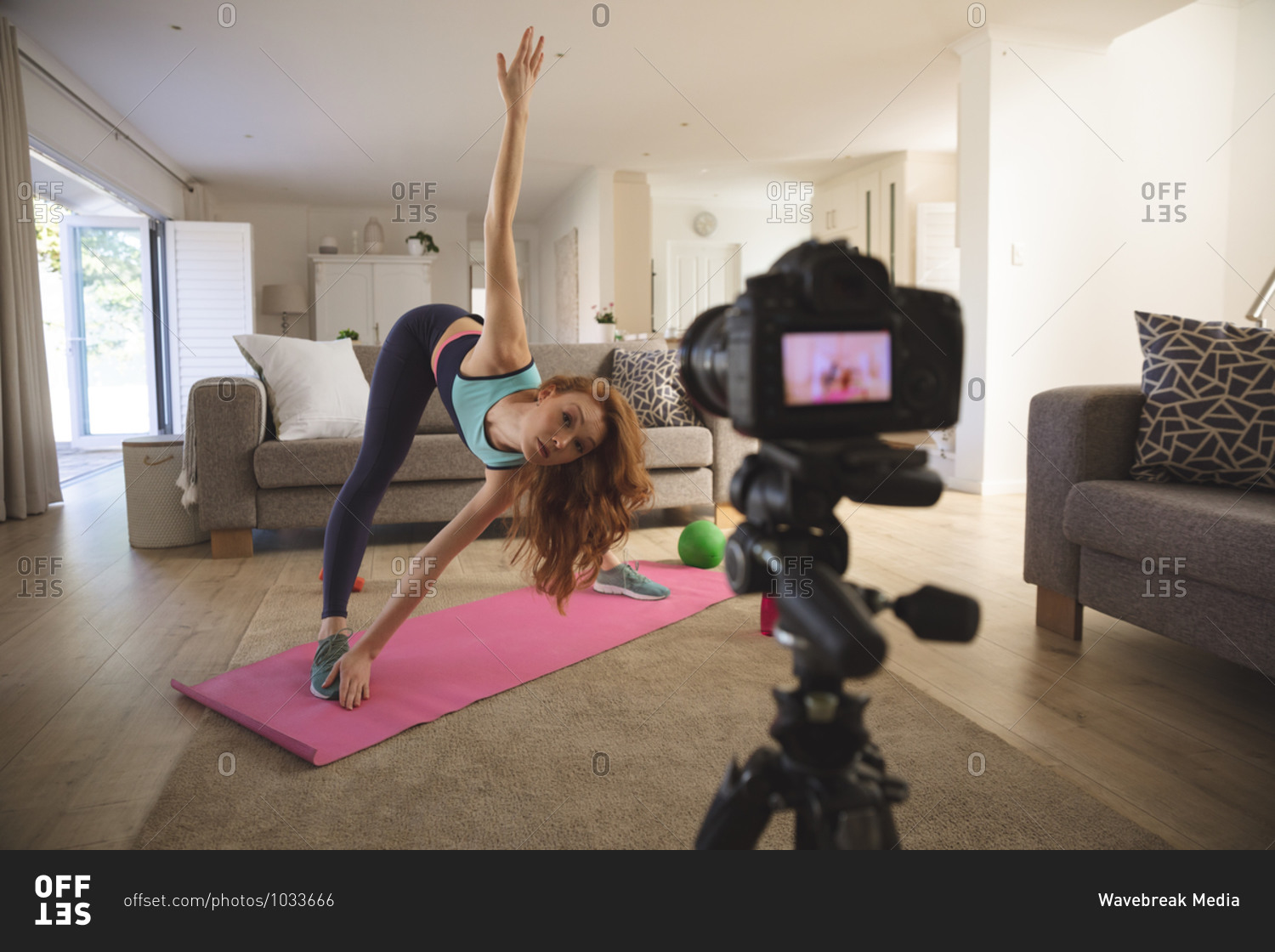 Caucasian woman spending time at home, in living room, exercising and recording it with a camera. Social distancing during Covid 19 Coronavirus quarantine lockdown.