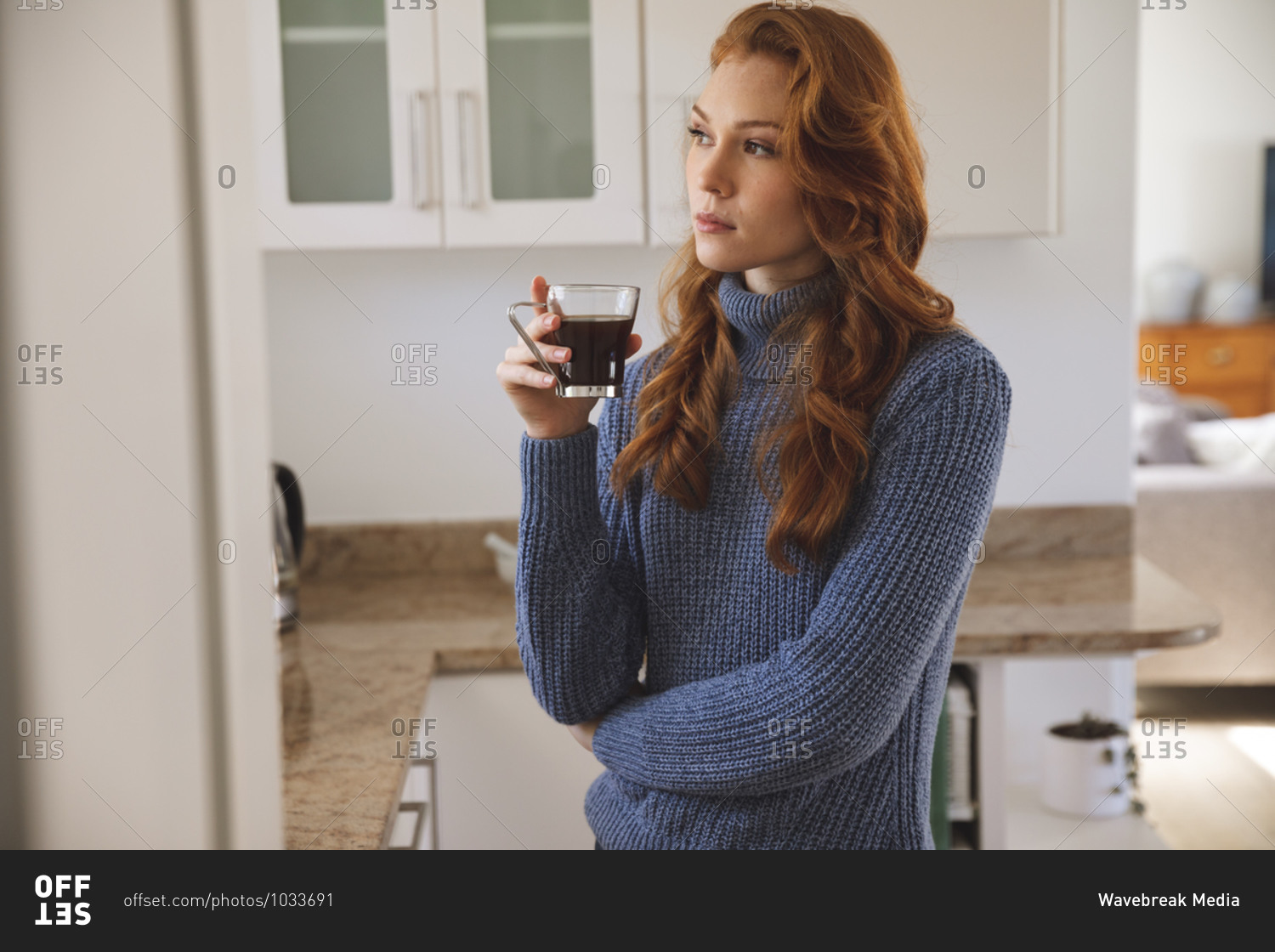 Caucasian woman spending time at home, in kitchen, looking serious, holding a cup, drinking coffee. Social distancing during Covid 19 Coronavirus quarantine lockdown.