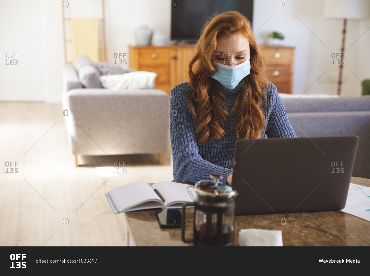 Caucasian woman spending time at home, in the kitchen, working from home, using her laptop,  wearing a face mask. Social distancing during Covid 19 Coronavirus quarantine lockdown.