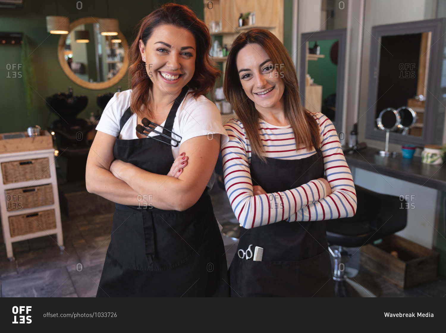 Portrait of two Caucasian female hairdressers working in hair salon, posing for a picture with their arms crossed. Health and hygiene in workplace during Coronavirus Covid 19 pandemic.