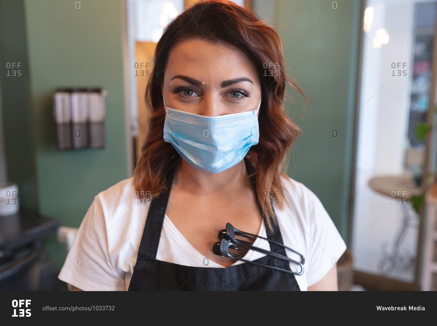 Portrait of Caucasian female hairdresser working in hair salon wearing face mask looking at camera. Health and hygiene in workplace during Coronavirus Covid 19 pandemic.