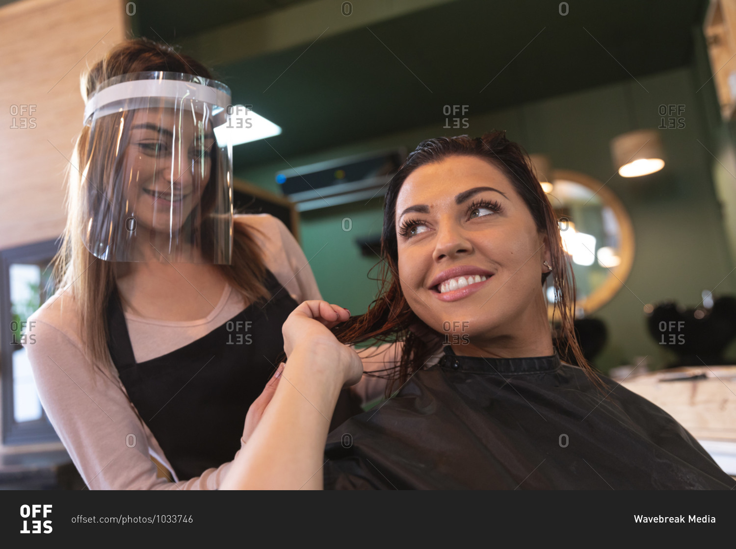 Caucasian female hairdresser working in hair salon wearing face cover, combing hair of female Caucasian customer smiling. Health and hygiene in workplace during Coronavirus Covid 19 pandemic.