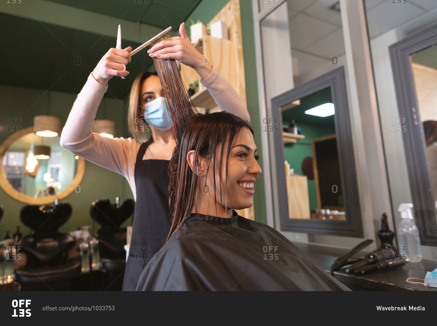 Caucasian female hairdresser working in hair salon wearing face mask, cutting hair of female Caucasian customer. Health and hygiene in workplace during Coronavirus Covid 19 pandemic.