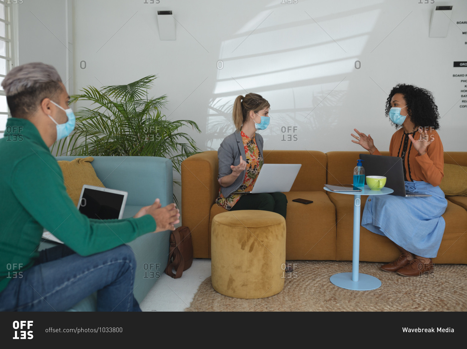 Multi ethnic group of male and female creatives wearing face masks and social distancing at a work meeting. Health and hygiene in the workplace during Coronavirus Covid 19 pandemic.