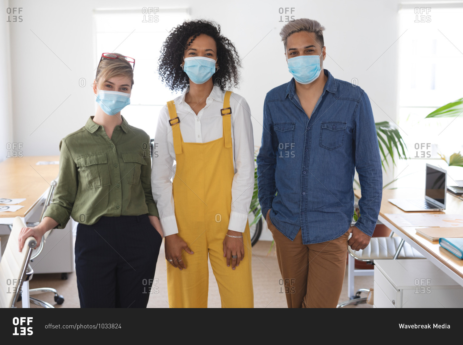 Portrait of a multi ethnic group of three male and female creatives in office wearing face masks, Health and hygiene in the workplace during Coronavirus Covid 19 pandemic.