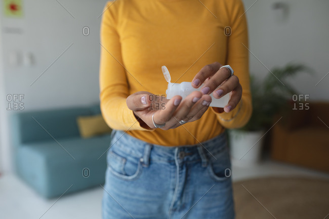 Mid section of mixed race woman standing in office disinfecting hands with hand sanitizer. Health and hygiene in workplace during Coronavirus Covid 19 pandemic.