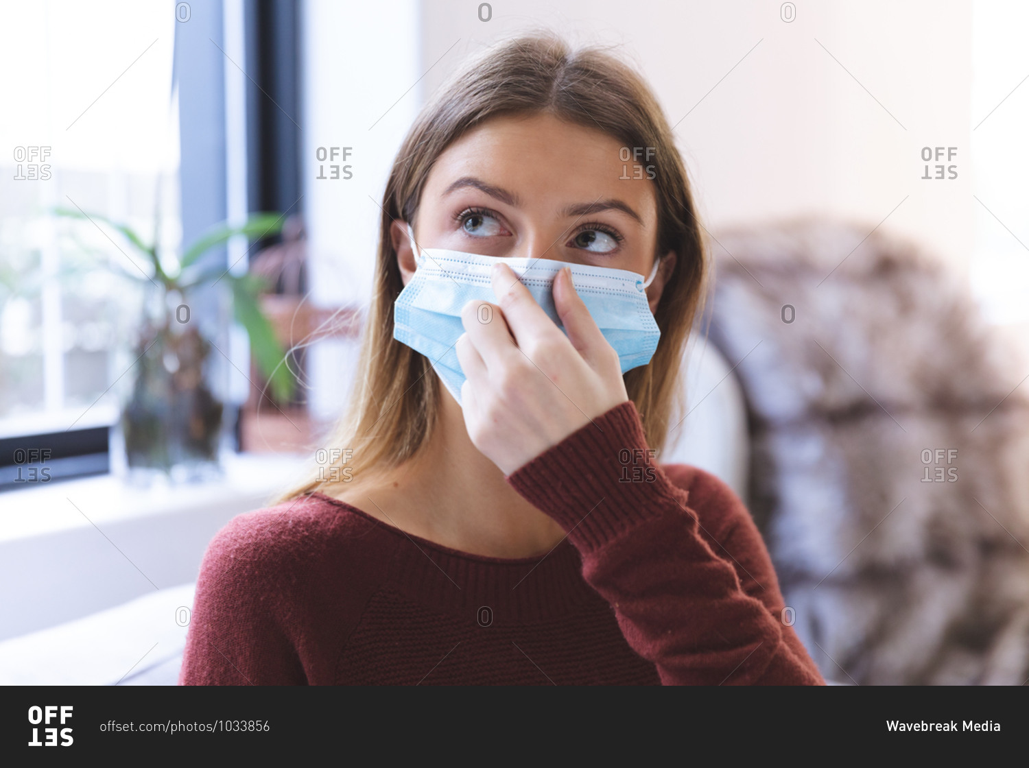 Caucasian woman spending time at home, sitting in living room, wearing face mask on. Social distancing during Covid 19 Coronavirus quarantine lockdown