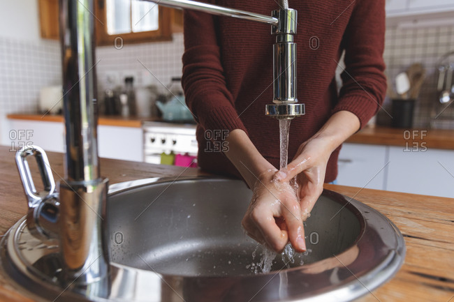 Mid section of Caucasian woman spending time at home, standing in kitchen washing her hands in basin. Social distancing during Covid 19 Coronavirus quarantine lockdown.