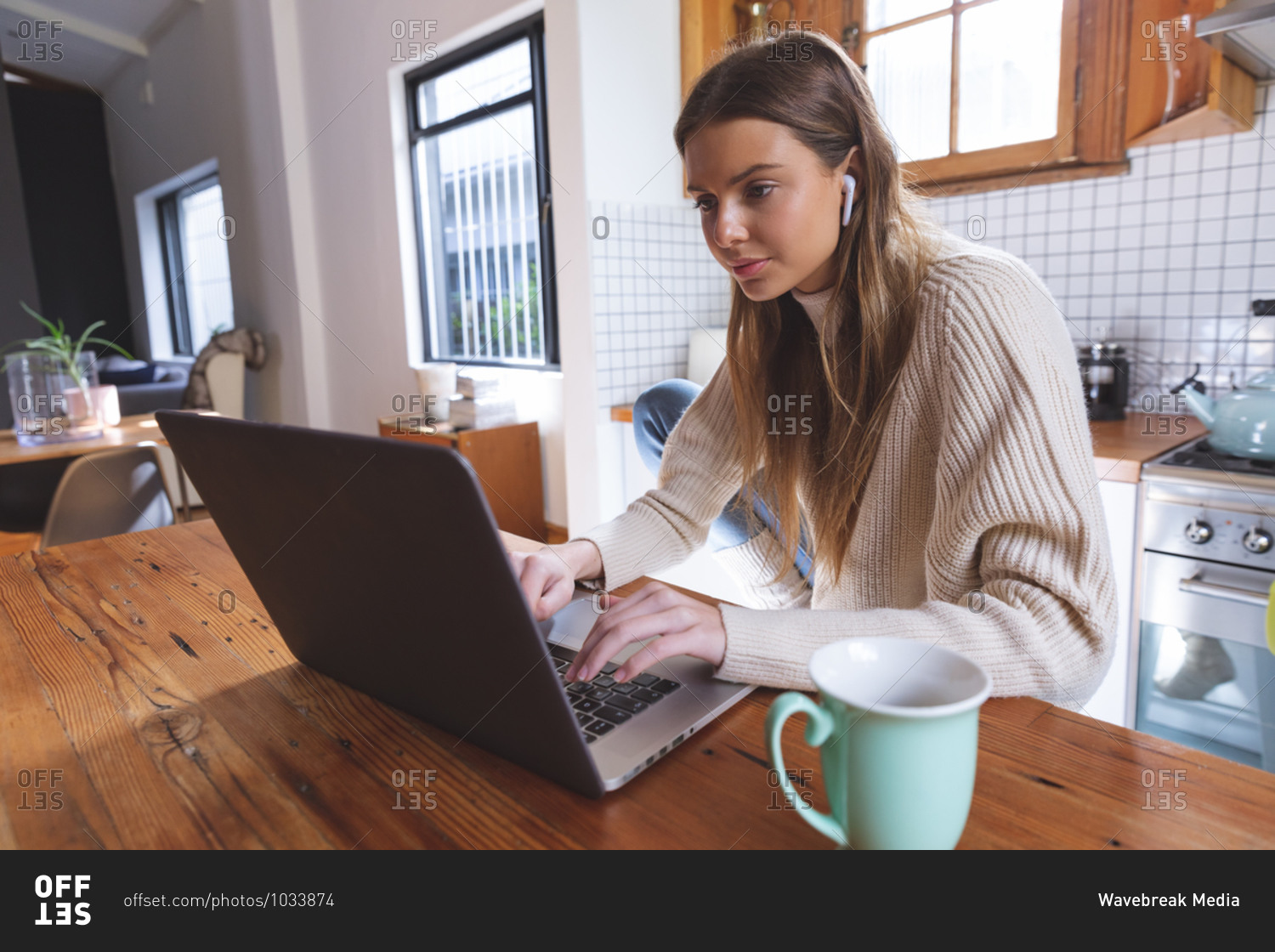 Caucasian woman spending time at home, sitting in kitchen using laptop computer with earphones on. Social distancing during Covid 19 Coronavirus quarantine lockdown.