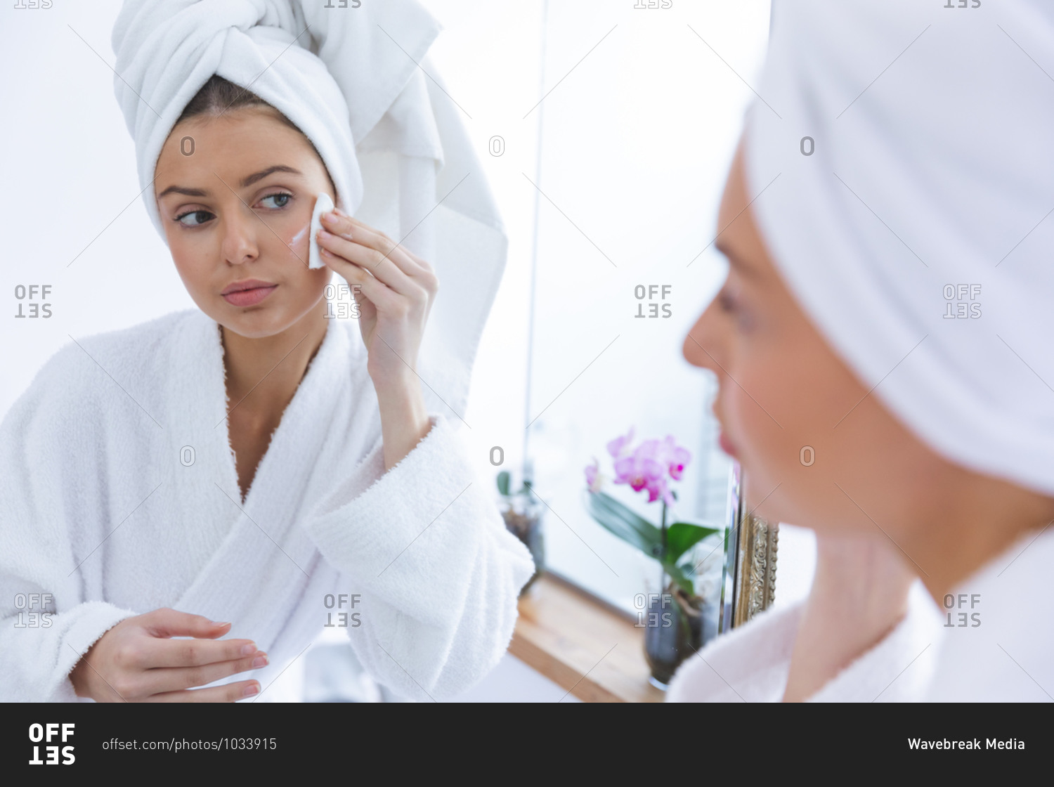 Caucasian woman spending time at home, standing in bathroom, looking in mirror removing make up with cotton pad. Social distancing during Covid 19 Coronavirus quarantine lockdown.