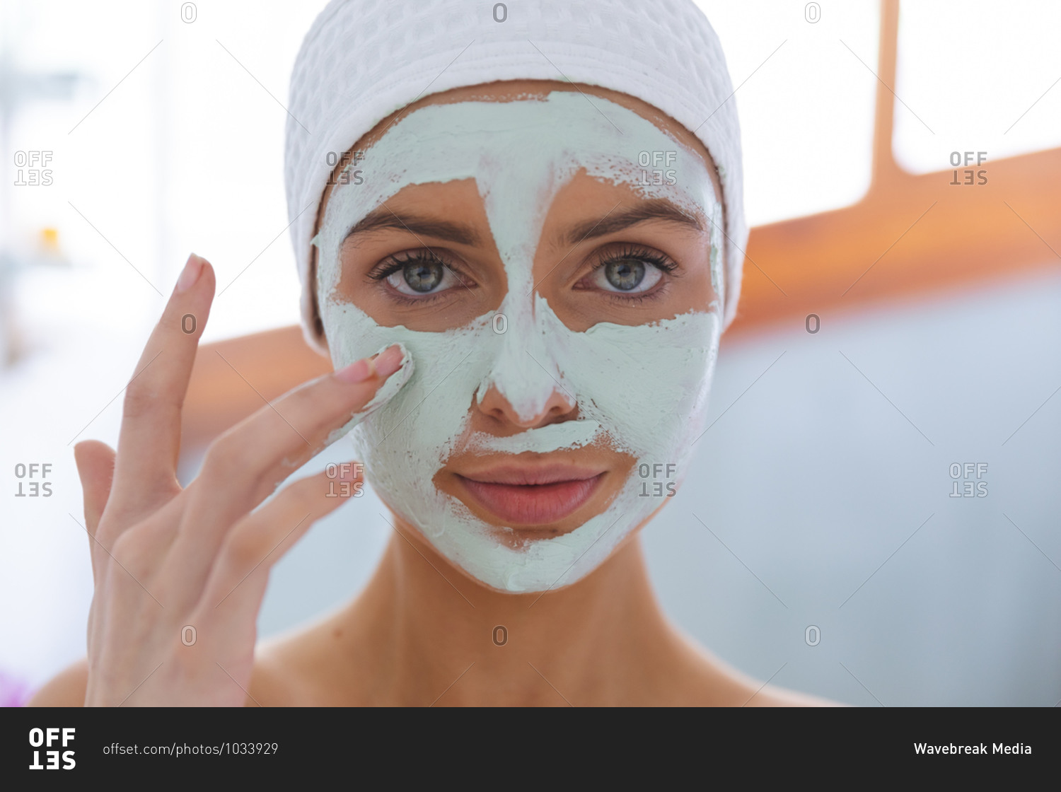 Portrait of Caucasian woman spending time at home, standing in bathroom, looking at camera applying face mask. Social distancing during Covid 19 Coronavirus quarantine lockdown.