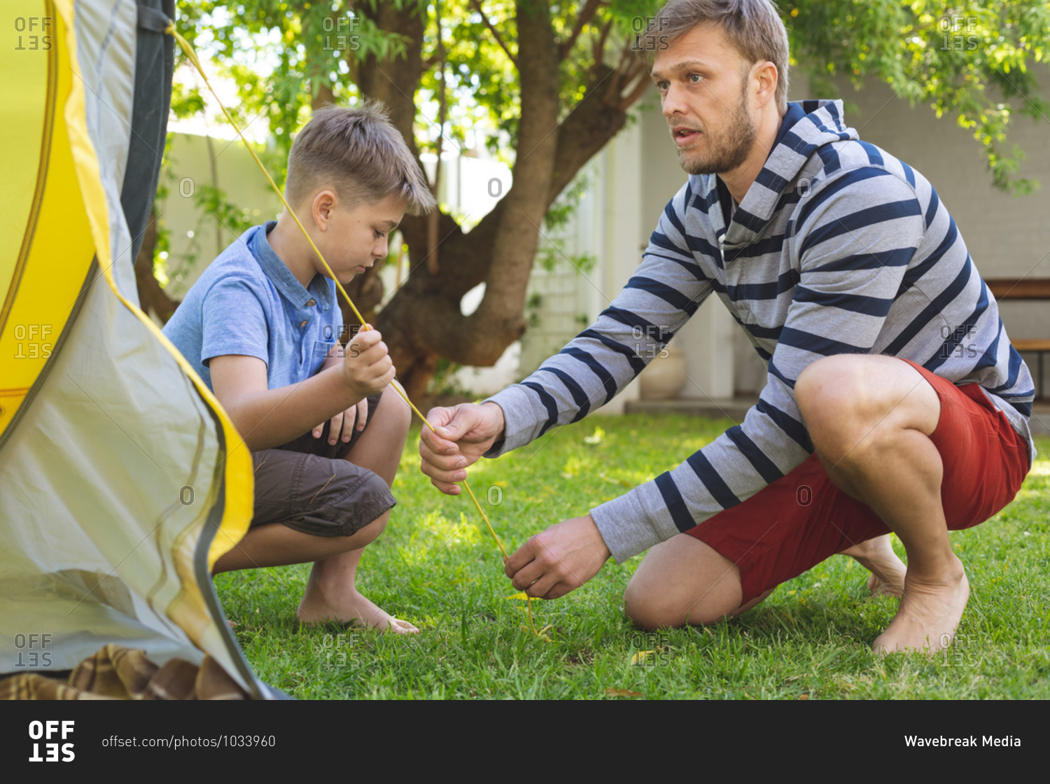 Caucasian man spending time with his son together, camping in garden, putting tent up. Social distancing during Covid 19 Coronavirus quarantine lockdown.