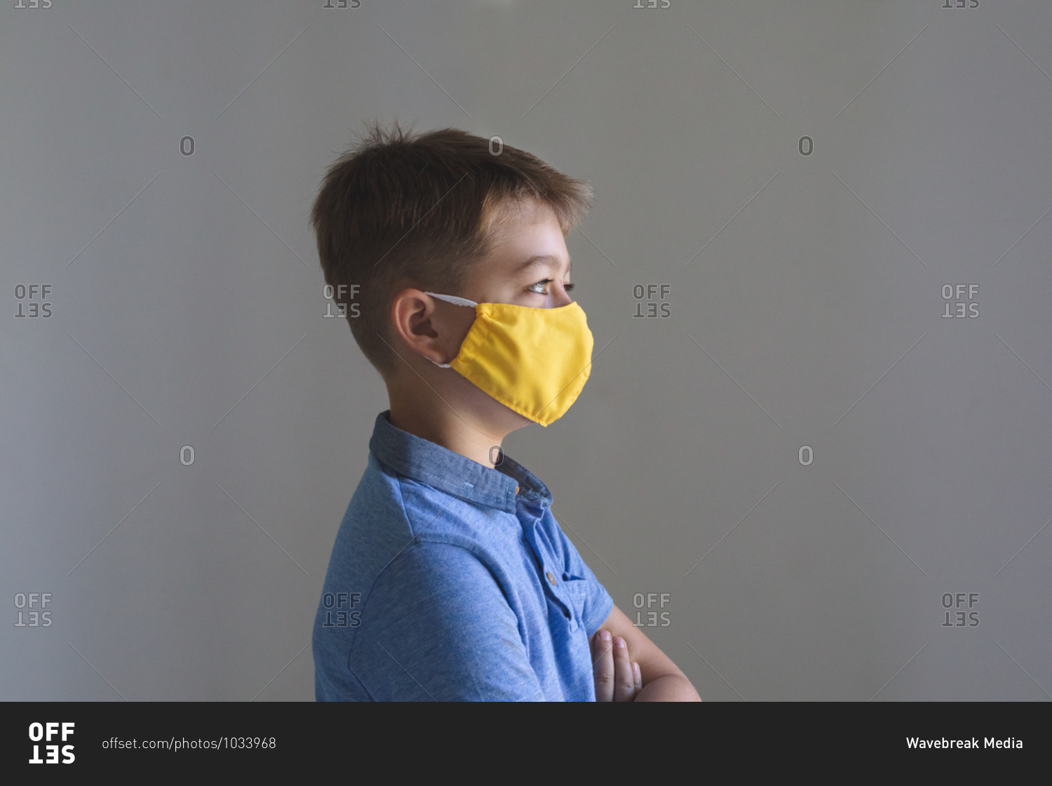 Side view of Caucasian boy spending time at home, wearing yellow face mask looking at camera on grey background. Social distancing during Covid 19 Coronavirus quarantine lockdown.