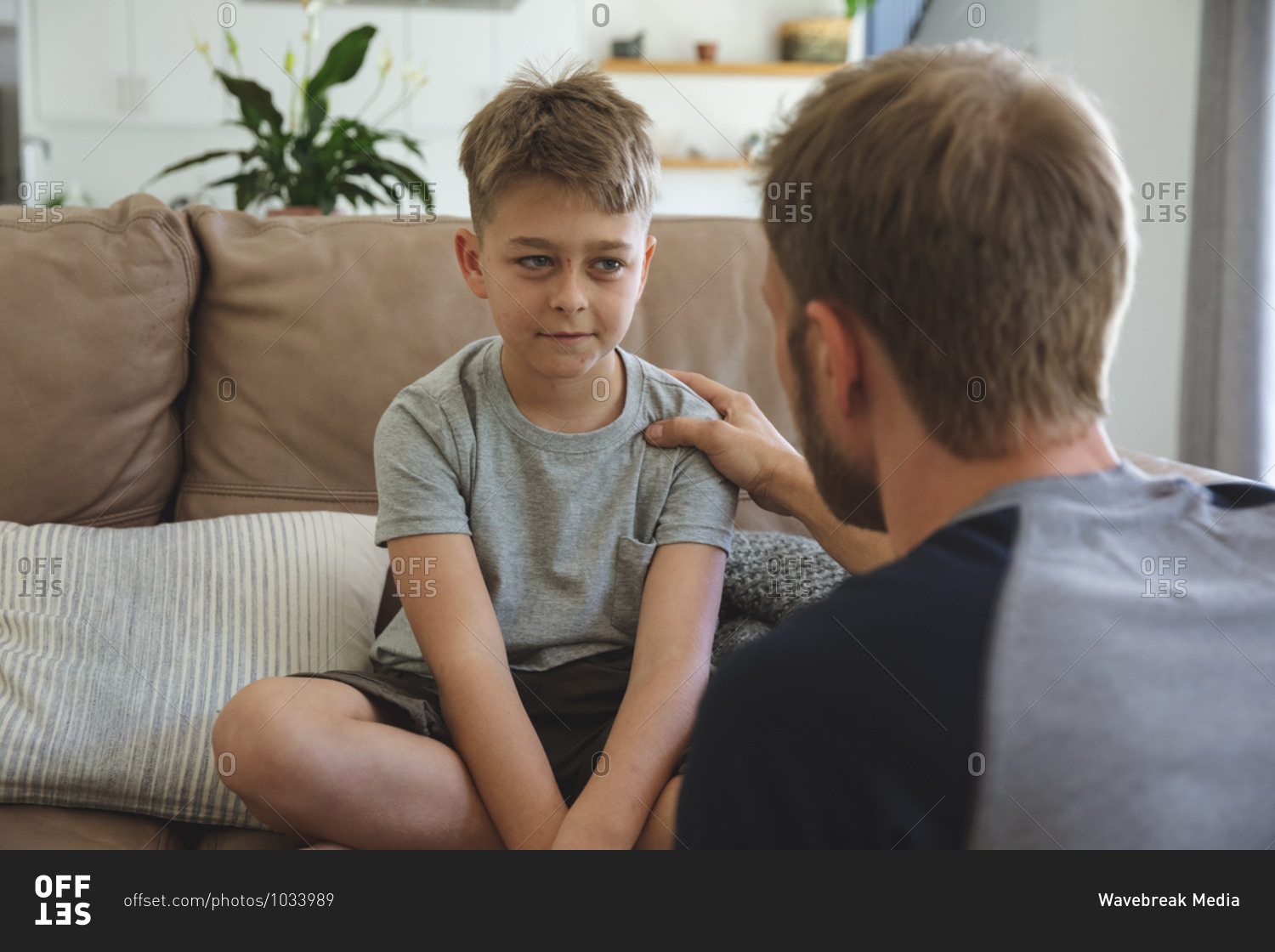 Caucasian man at home with his son together, sitting on sofa in living room, talking to each other. Social distancing during Covid 19 Coronavirus quarantine lockdown.