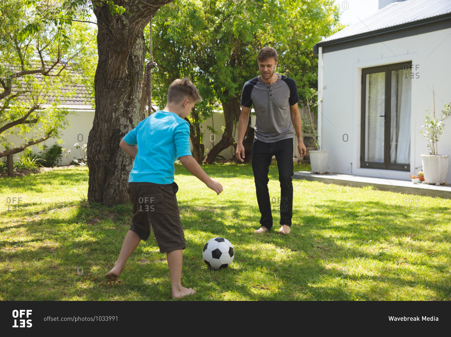 Caucasian man spending time with his son together, playing football in garden. Social distancing during Covid 19 Coronavirus quarantine lockdown.