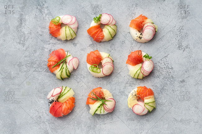 Top view of sushi donuts with salmon and veggies on gray background