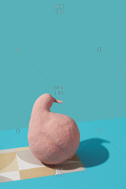 A pink painted pumpkin on a piece of paper with geometrical pattern against blue background with copy space