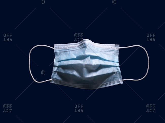 Disposable, surgical mask floating on navy blue background