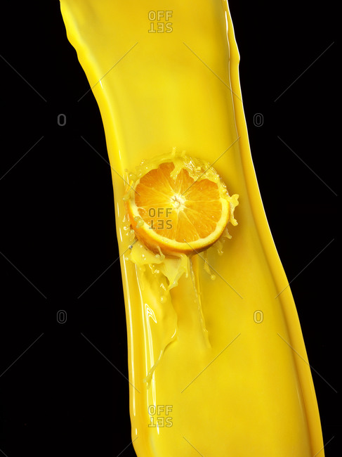 Orange in an orange juice splash against a black background